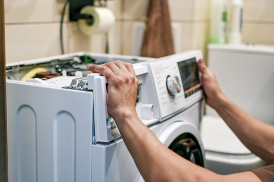 A front-loading washing machine repair in progress. The technician (or owner) is performing maintenance at home, judging by the bathroom setting in the background.