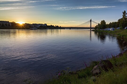 Midsummer night, midnight sun at the river Kemijoki, suspension bridge lumberjack candle bridge and mobile homes on the horizon, backlight, Rovaniemi, near Arctic Circle, Lapland, Finland