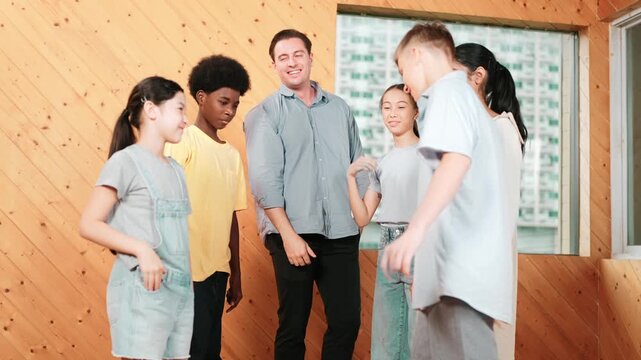 Caucasian teacher and happy diverse children putting hand together to celebrate successful project while standing circle. Represent love, corporate, team working, togetherness and unity. Edification
