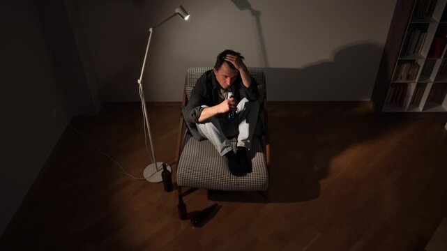 Young man sits on floor in a dark room drinking from a beer bottle, isolated and struggling with depression, alcoholism and the heavy weight of loneliness