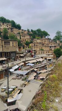 Panoramic view of the historic terraced mountain village of Masouleh featuring rooftop cafes, traditional clay houses and local market, panning shot from left to right, vertical 9:16 video.