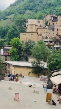 Historic terraced mountain village of Masouleh with traditional clay houses, busy local shops and tourists, panning shot from right to left, vertical 9:16 video.