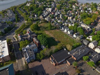 Fototapeta premium Aerial drone view of Salem Common park and Salem, Massachusetts, showing green grass, walking paths, historic neighborhood houses, and the scenic North River in the background on a sunny summer day