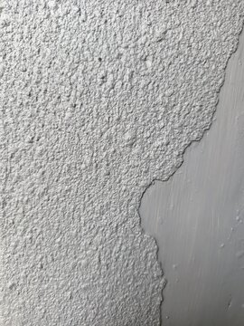 The image shows a high-contrast texture of a grey textured stucco ceiling or wall meeting a smooth, painted grey plaster surface along an irregular edge.