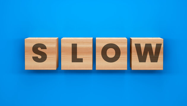 Wooden Blocks Spell Slow: Four wooden blocks arranged on a vibrant blue surface spell out the word SLOW, symbolizing a deliberate pace or a period of inactivity.