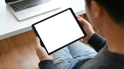 Naklejka premium Person holding tablet with blank screen and laptop on white desk in modern home workspace