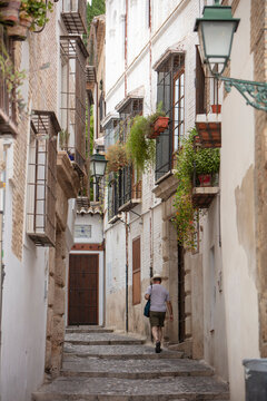 A male tourist with shorts and a hat is walking the historic cobblestone streets of Spain