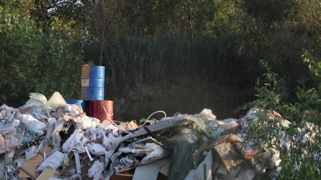 Close-up of illegal garbage dump with barrels and lush trees. This footage highlights environmental damage and waste management challenges in an outdoor setting.