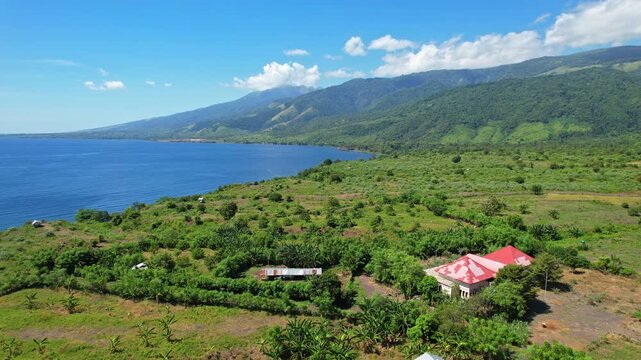 Aerial drone footage of a vast plain on the edge of Tambora national park volcano mountain, from the north side, with foreground mountain slopes and blue sea, in Sumbawa island, Indonesia
