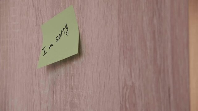 Close-up of hand sticking I'm sorry apology sticker on wooden panel. Video footage of requests for forgiveness and reconciliation.