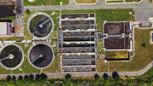 Overhead view wastewater treatment plant with circular clarifiers, linear aeration lanes, adjacent access roads and green perimeter technician role monitoring