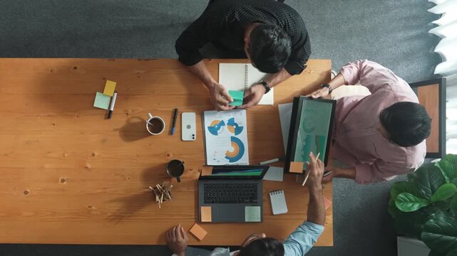 Smart project manager calling phone while diverse team brainstorm idea and looking at financial statistic at tablet at meeting table. Diverse business people planning marketing strategy. Convocation.