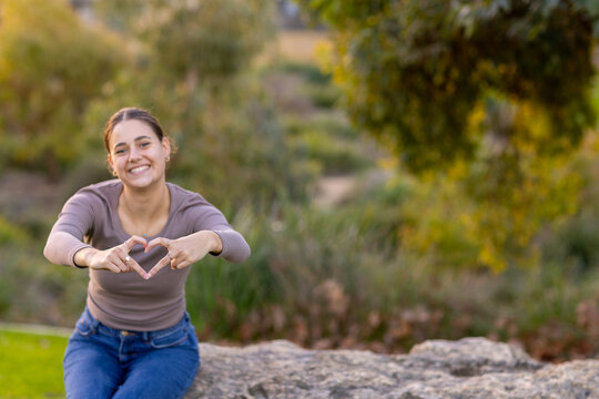 teen girl leaning forward and making a heart shape with her fingers