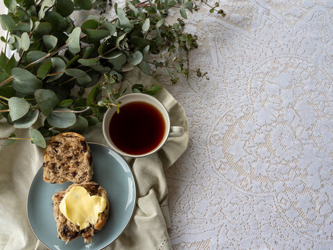 Hot Cross Bun on a plate with a cup of tea and eucalyptus branch