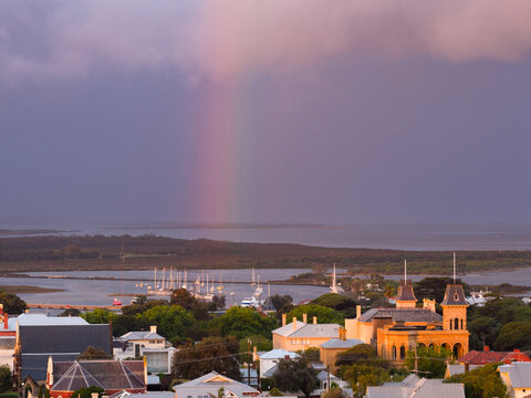 Aerial view of a rainbow in a dramatic coloured sky over historic buildings in a coastal town
