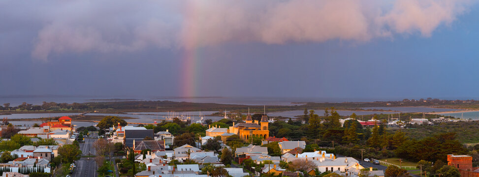 Aerial view of a rainbow in a dramatic coloured sky over historic buildings in a coastal town