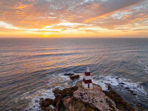 Aerial view of a golden sunset sky over an obelisk monument on a rocky coastal cliff top