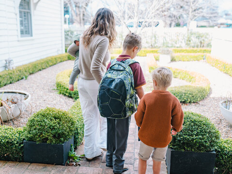 Aussie mum walking son with backpack on front porch while carrying toddler son on hip
