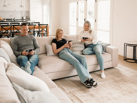 Family of three sitting comfortably on the couch while on their phones
