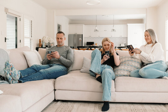 Family of three sitting comfortably on the couch while on their phones