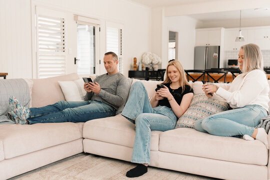 Family of three sitting comfortably on the couch while on their phones