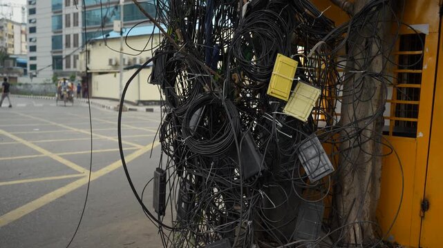 Dhaka, Bangladesh - 14 May 2026: View of a massive tangle of electrical and telecommunication cables hanging over a city street with buildings and a car in the background.