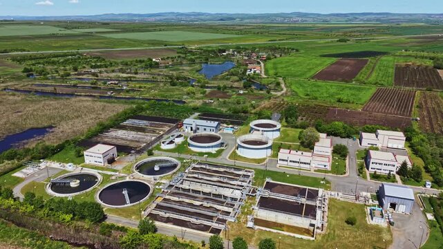 Aerial industrial wastewater recycling facility showcasing multiple circular clarifiers, oxidation basins, solar panels, access roads, nearby farmland,