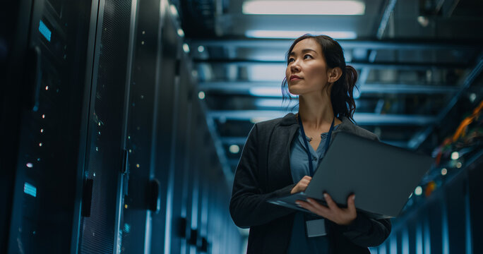 Technician uses a laptop computer to check and monitor server racks in a large data center, hardware installation, network devices diagnosttics, system check. Server room with mainframes.