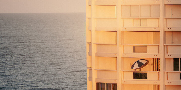 Beach umbrella on balcony of modern apartment building overlooking the calm ocean at sunset