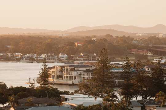 Luxury waterfront mansions nestled among trees at sunset with hazy mountains in background