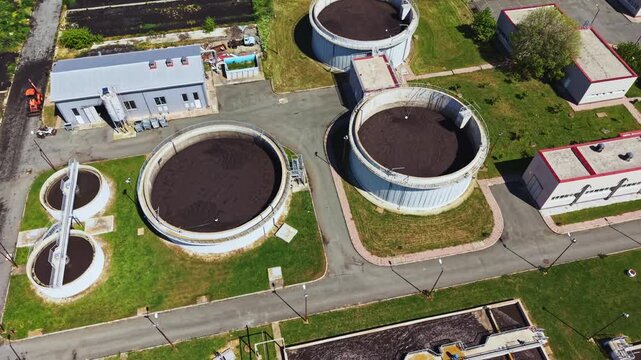 Aerial view wastewater treatment plant showing circular tanks, clarifiers, sludge digesters, piping and settling basins, drone survey perspective with utility