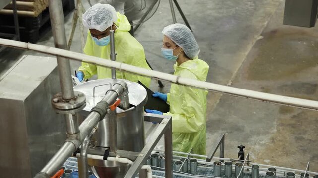 Supervisory team wearing PPE meticulously inspects the mackerel or sardine production line from canning to tomato sauce filling on conveyor belts in industrial seafood processing plants.