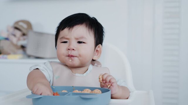 Asian Baby Using Finger to Feed Herself a Food with Baby Led Weaning Concept.Cute Asian baby boy eating finger food in high chair.