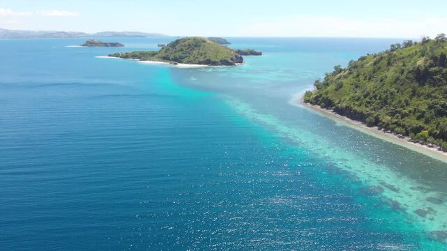 Panoramic aerial view of the 17 Islands Marine Park near Riung, Flores, Indonesia, featuring turquoise coral reefs, tropical islets, and deep blue ocean under a bright sky