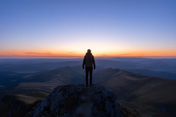 Fototapeta premium Lone hiker silhouetted on mountain peak at sunrise, vast landscape