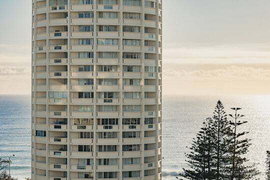 Tall cylindrical apartment building overlooking the sparkling ocean with pine trees in foreground