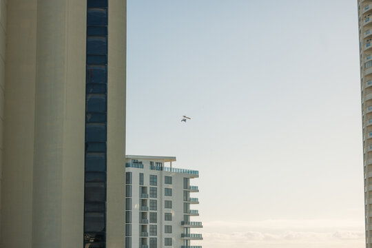 Ultralight aircraft soars high above modern buildings against a clear sky on the Gold Coast