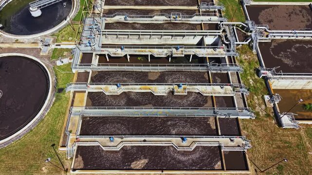 Aerial view sewage treatment plant basins showing series of rectangular aeration tanks and circular clarifiers, brown sludge surfaces, rotating mixers, visible