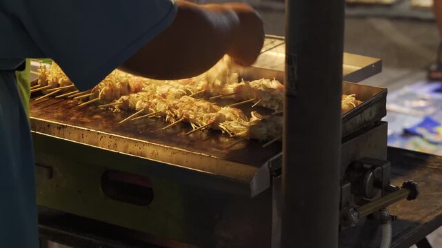 Close-up of bacon wrapped enoki mushroom skewers cooking on a flat top grill at a street food market.