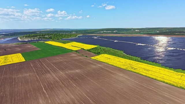 Aerial view shows yellow wildflowers and green fields alongside solar panels near a river. Bright sunlight reflects off the panels, highlighting the landscape in good weather.