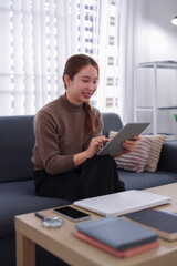 young Asian businesswoman entrepreneur using digital tablet device working from home sitting on sofa planning strategy research online business meeting remote © snowing12