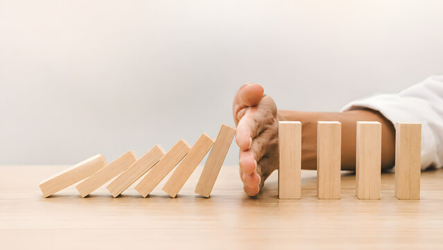 Hand stopping falling wooden domino blocks chain reaction concept for risk management crisis intervention protection insurance prevention strategy stabilization solution mitigation problem solving
