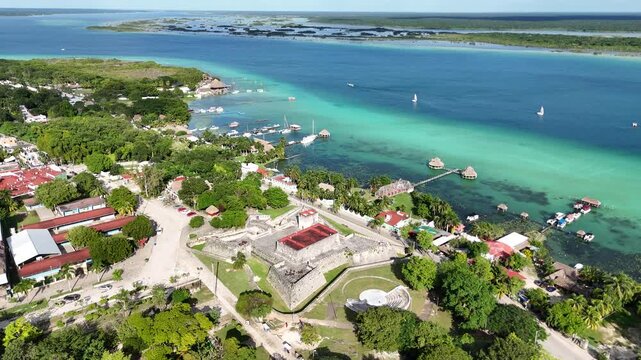 BACALAR, MEXICO: Aerial drone shot of the turquoise Lagoon of Seven Colors, capturing scenic wooden piers, docks with boats, waterfront resorts with thatched roofs and clear gradient water.