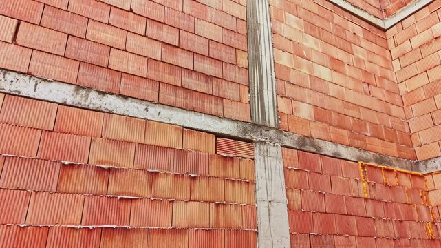 Exposed terracotta brick corner with concrete beams and visible mortar joints, unfinished interior shell showcasing clay block texture and rugged grain, warm