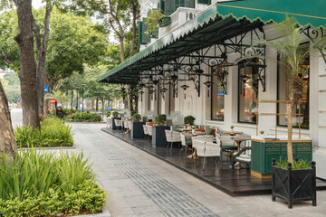 Fototapeta premium Elegant outdoor cafe seating on a sidewalk with French colonial architecture in Hanoi, Vietnam