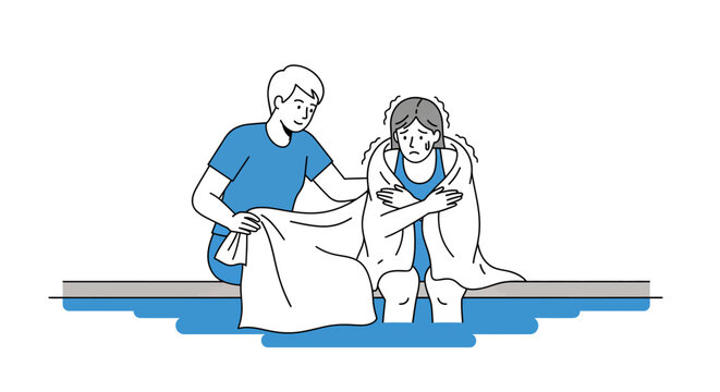 Caring man covering shivering cold woman with a blanket near water