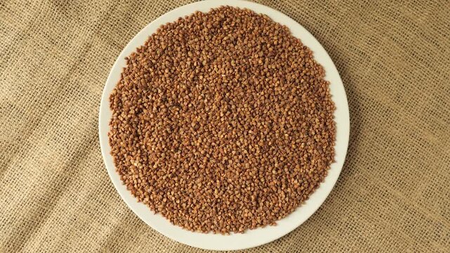 White plate with buckwheat groats rotating on burlap fabric