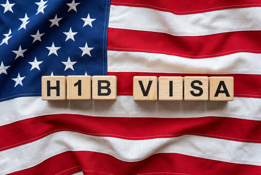 Wooden cubes spelling h1b VISA resting on a naturally draped american flag