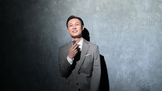 グレー背景で笑顔でプレゼンをする日本人男性