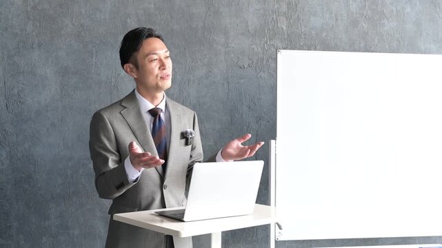 グレー背景でプレゼンをするスーツを着た日本人男性